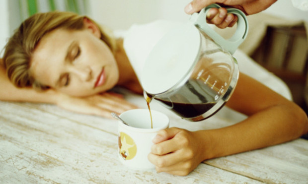 Woman asleep at table holding mug, man pouring coffee into mug