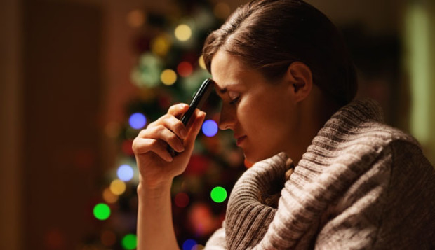 Concerned young woman with mobile phone in front of christmas tree