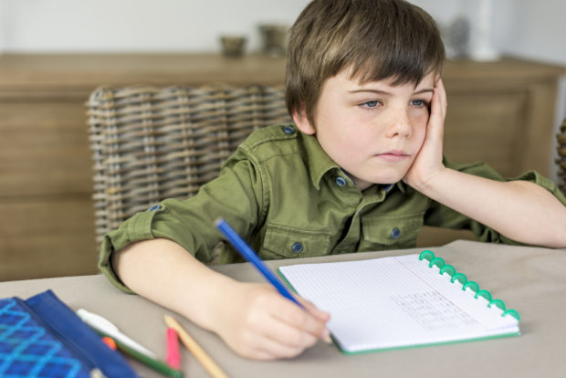 boy doesn't feel like making homework with hand under his head